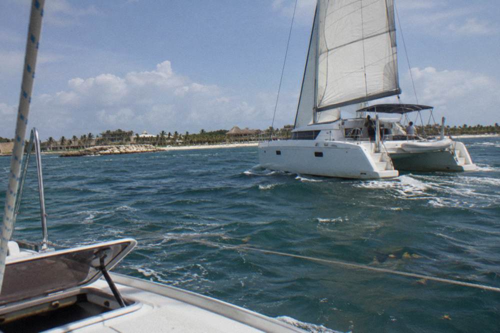 A private catamaran under sail on open water away from the coastline with a clear sky above