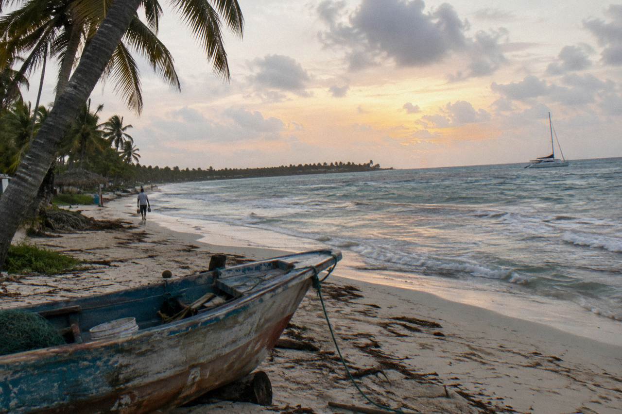 Calm Caribbean water in soft evening light along a palm-lined shore with an anchored catamaran in the distance