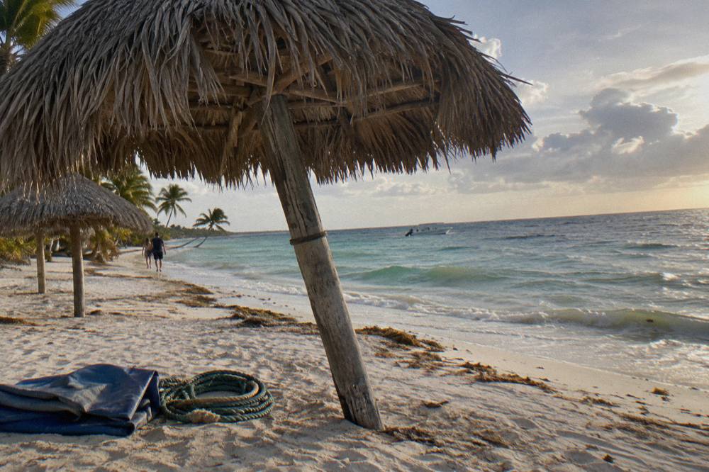 Empty thatched beach palapas on white sand beside calm shallow turquoise sea