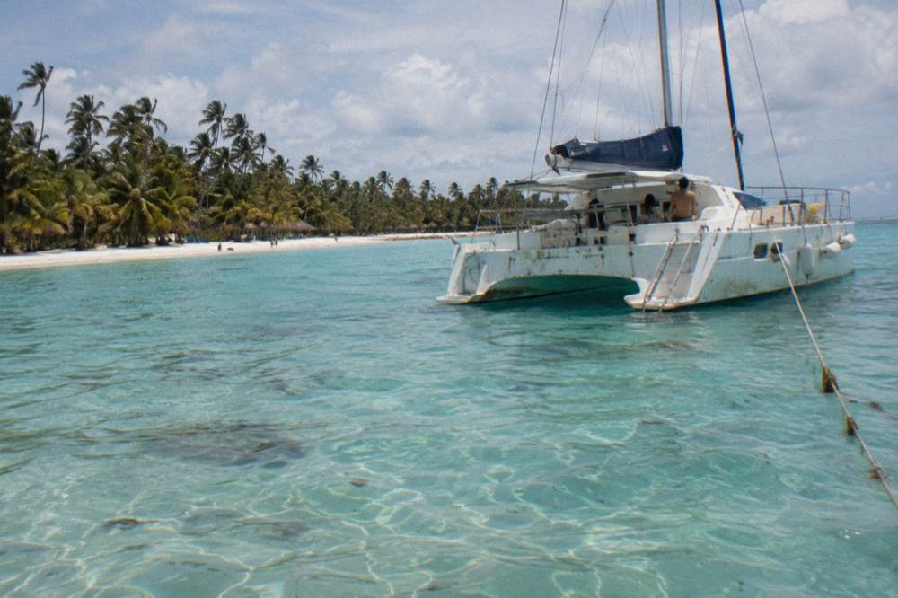 Private catamaran anchored in clear shallow water near a palm lined beach