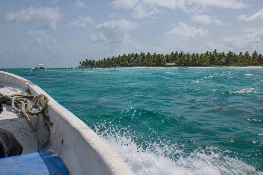 A speedboat crossing open turquoise water with distant palm-covered island shoreline