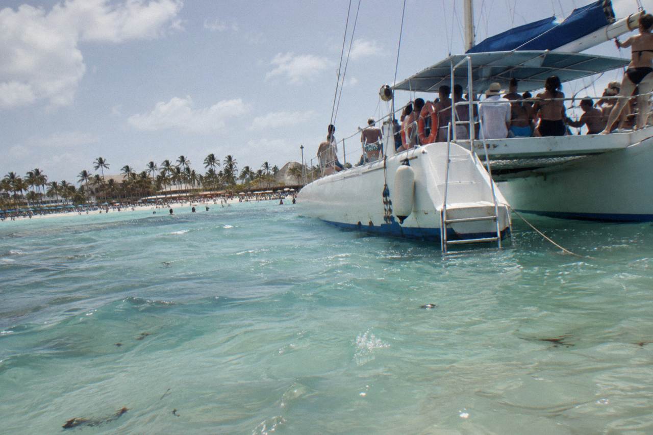 A large catamaran anchored in shallow turquoise water near a natural sandbar