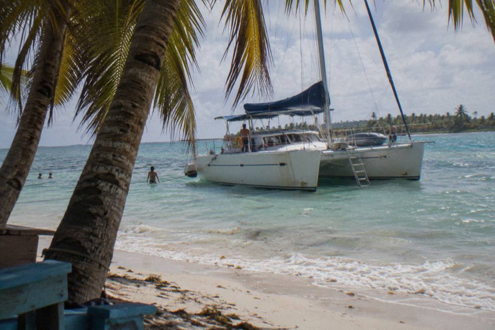 A catamaran moored in clear shallow water beside a sandy Caribbean beach
