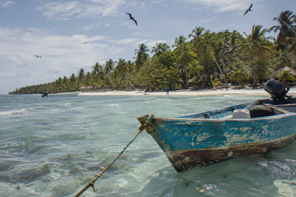 A wooden boat anchored off a palm-lined island shoreline at midday
