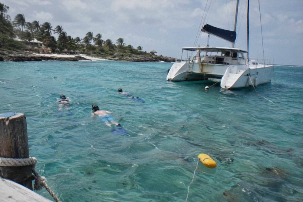 Snorkelers in calm turquoise water beside a moored catamaran