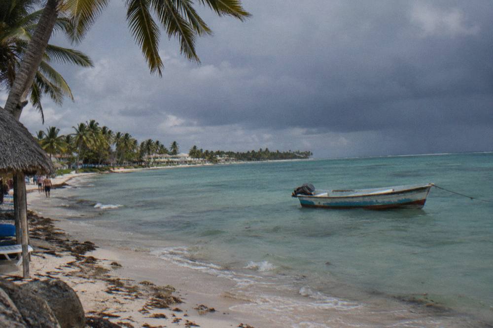 Dark rain clouds over calm turquoise water along a palm-lined shore