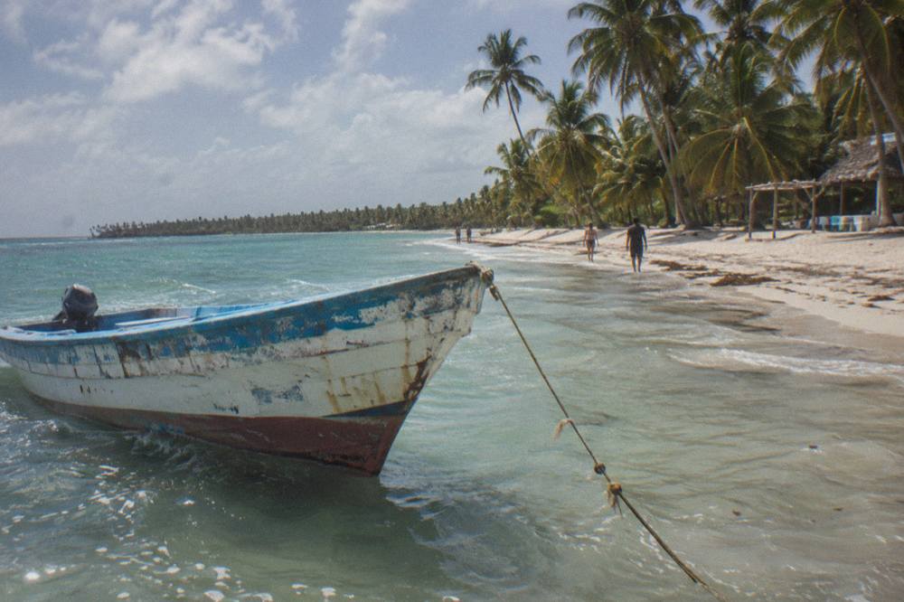 A wooden speedboat anchored beside a wide palm-lined beach of pale sand
