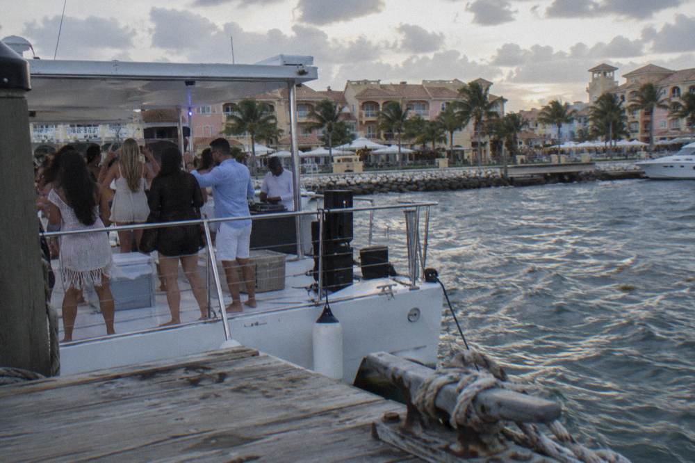 Group of adult guests dancing on a boat deck with a DJ booth and speaker setup