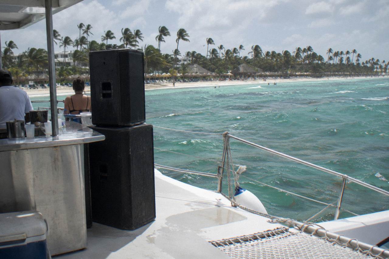 Catamaran deck with music speakers and open bar counter at anchor off a palm-lined Caribbean beach