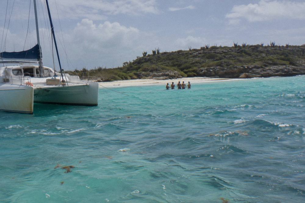 Catamaran moored at a shallow sandbar with guests standing in waist-deep turquoise water