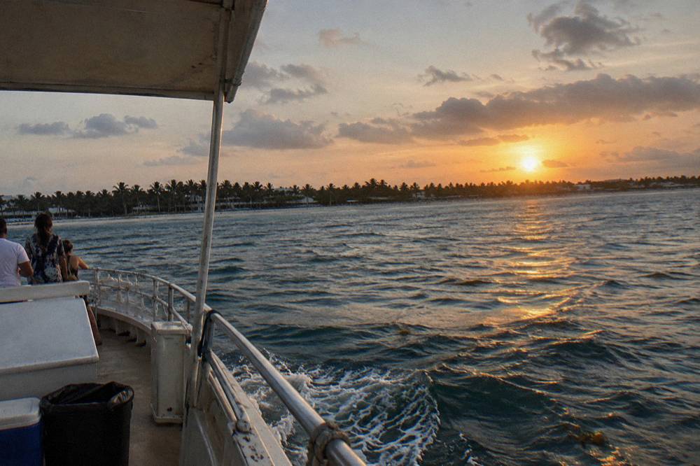 Boat deck at golden hour with calm sea and distant palm-lined shoreline