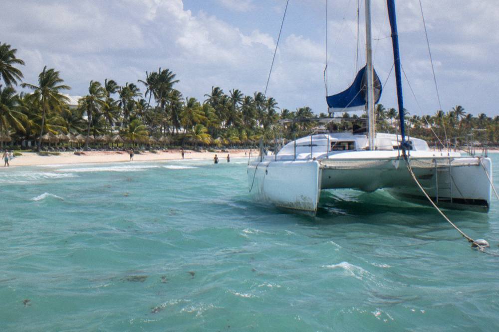 Catamaran anchored in shallow turquoise water near a sandy beach with palms