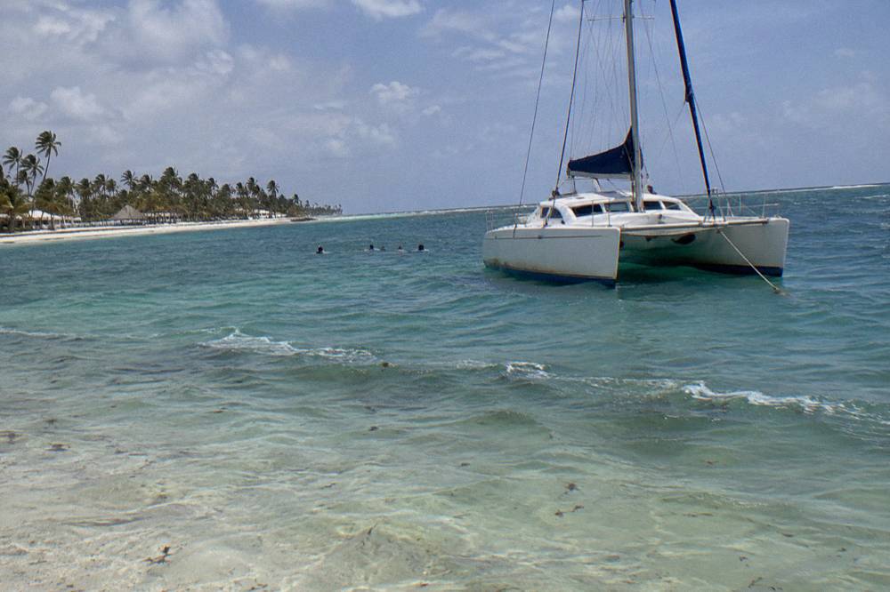 Snorkelers in the water beside a moored catamaran over a sandy bottom