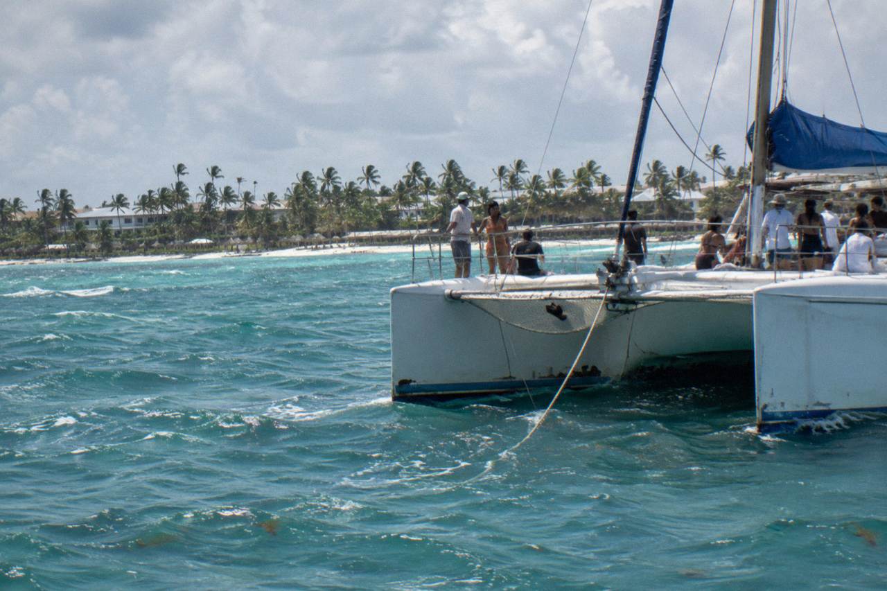 Catamaran with passengers dancing beside turquoise water along the Bavaro coast