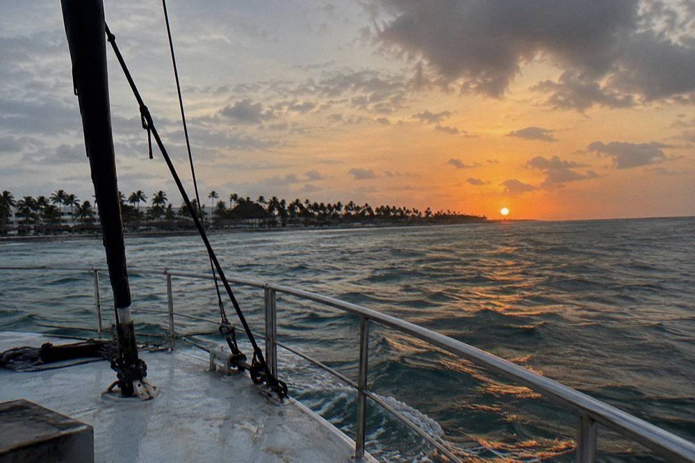 A boat deck at golden hour with the sun low over calm Caribbean water