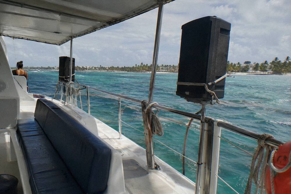 Open deck of a catamaran with speakers and a shaded seating area on calm turquoise water