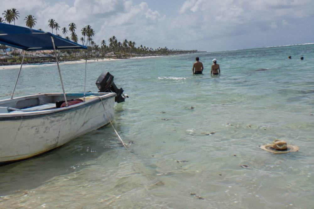 Boat anchored at a shallow sandbank with people standing in clear waist-deep water