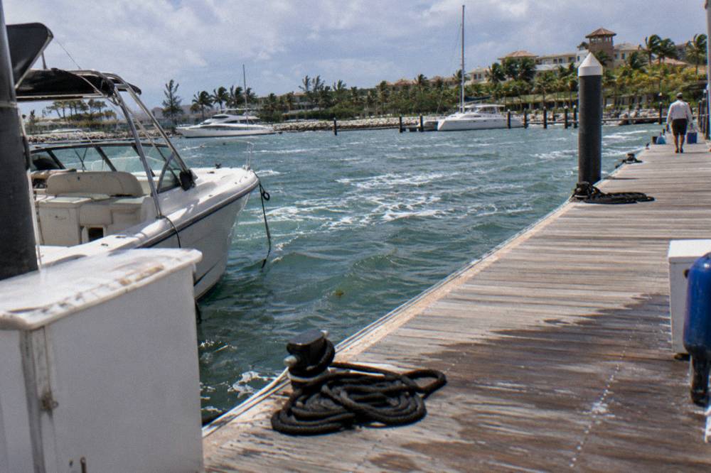 Beach bag with towel, sunscreen and sunglasses on a wooden dock beside a boat