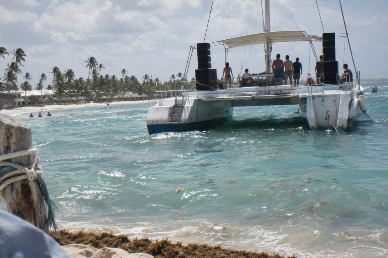 Catamaran with speakers and dancing deck anchored off a palm-lined Caribbean beach
