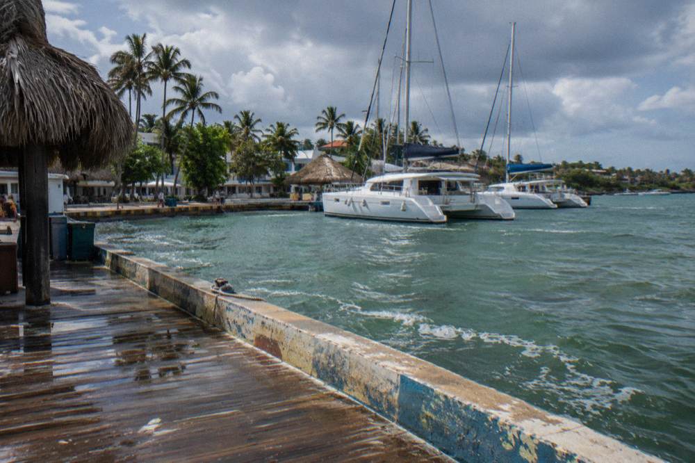 Wooden dock with moored catamarans at a Bayahibe marina under clearing skies