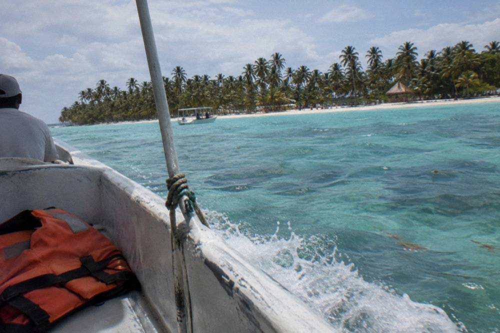 Speedboat crossing turquoise shallow water toward Saona Island with palm trees visible