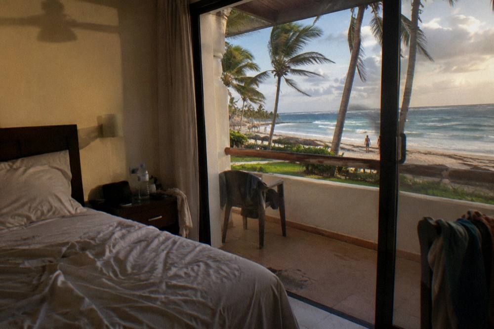 Traveler packing sunscreen, hat and sunglasses on a hotel room bed before a boat excursion