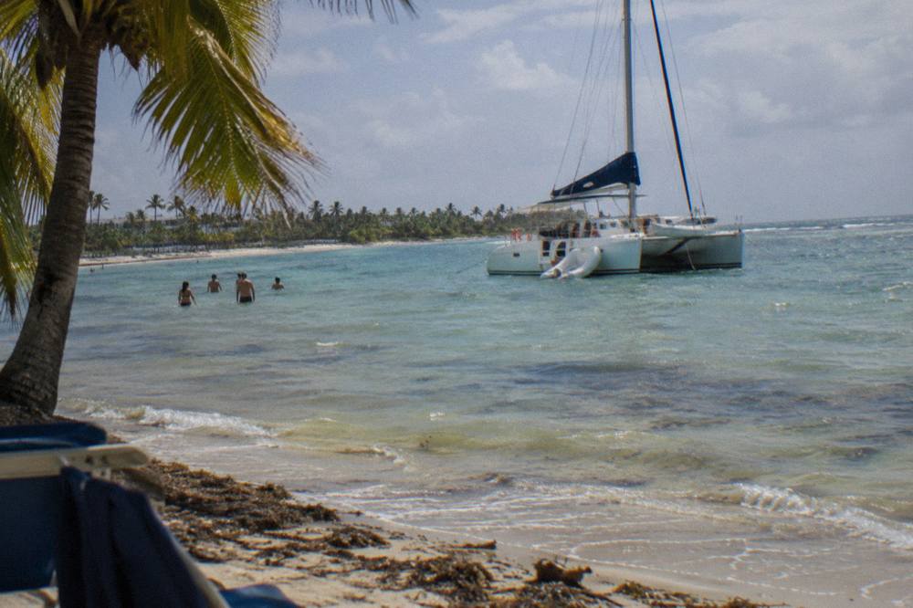 A catamaran anchored beside a shallow sandbar with guests standing in clear water