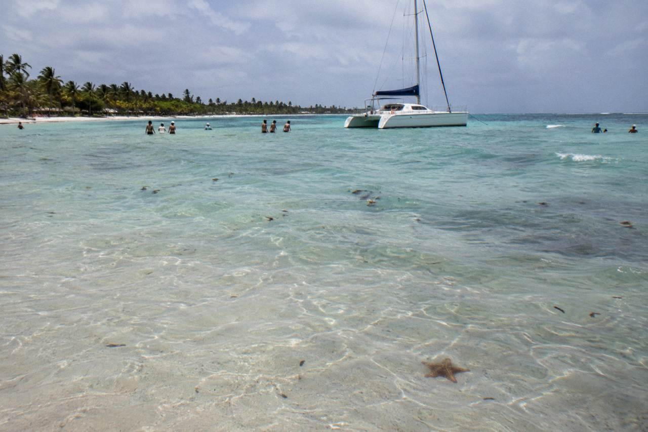 Shallow turquoise water over a sandy shoal with a moored catamaran in the distance