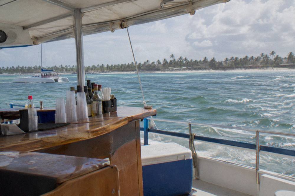 Crew member pouring rum cocktails at an open bar counter on a catamaran deck