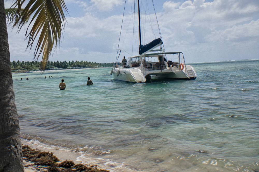 Catamaran anchored at a shallow natural pool with guests standing in the water