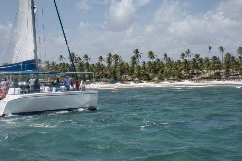 Open-air catamaran cruising along a palm-fringed coastline in morning light