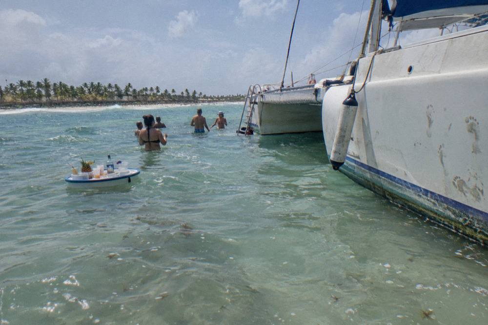 Catamaran moored at a shallow sandbar with guests standing in waist-deep turquoise water