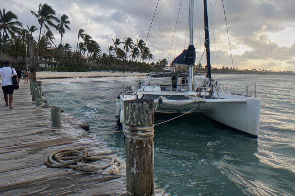 Wooden dock at a Bavaro beach with a catamaran tied up and palm trees along the shore