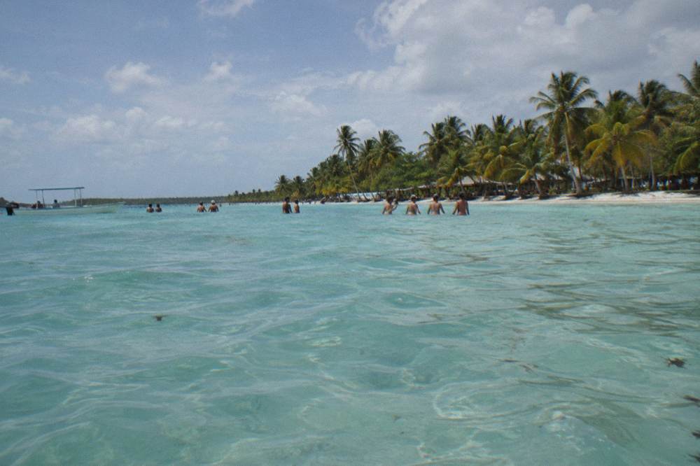 Guests standing in waist-deep water at a natural sandbar pool