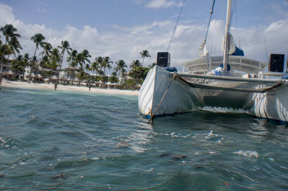 Private catamaran with netted deck and music speakers moored off a white sand beach