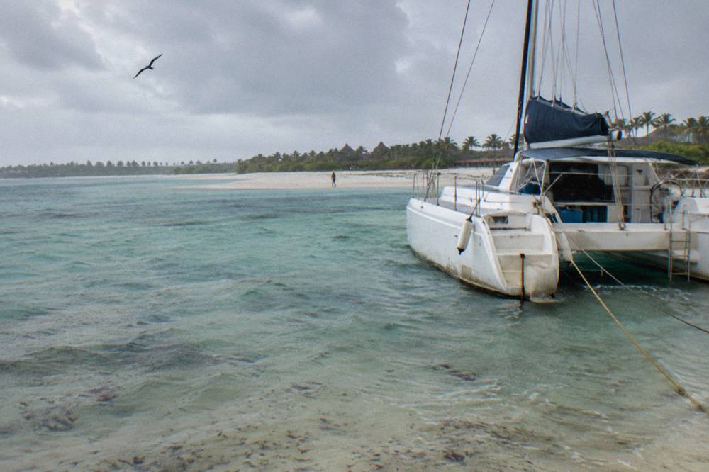 A private catamaran moored in clear shallow water with a sandbar behind it