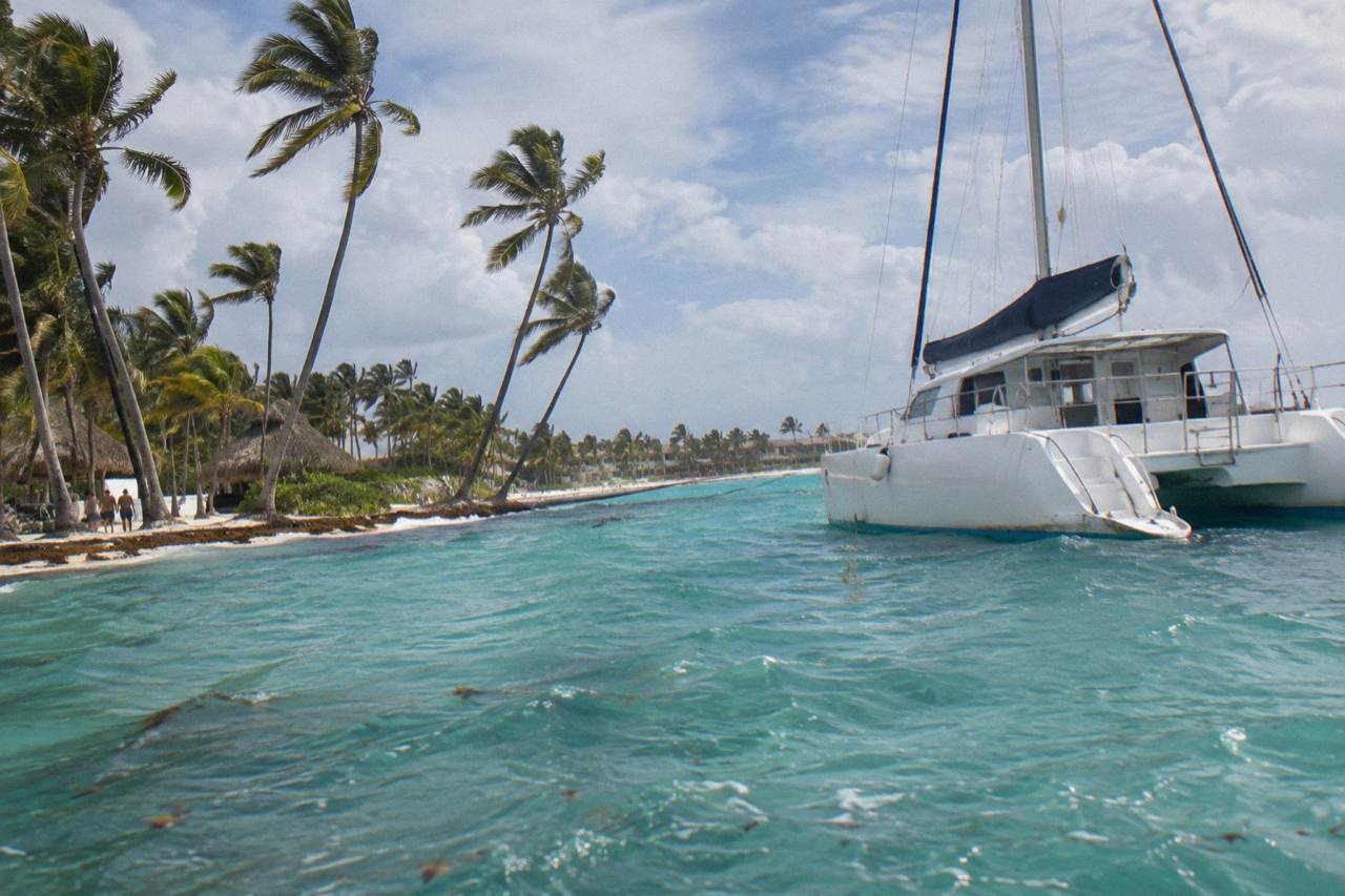 A catamaran anchored off a Caribbean beach with turquoise water and palm trees