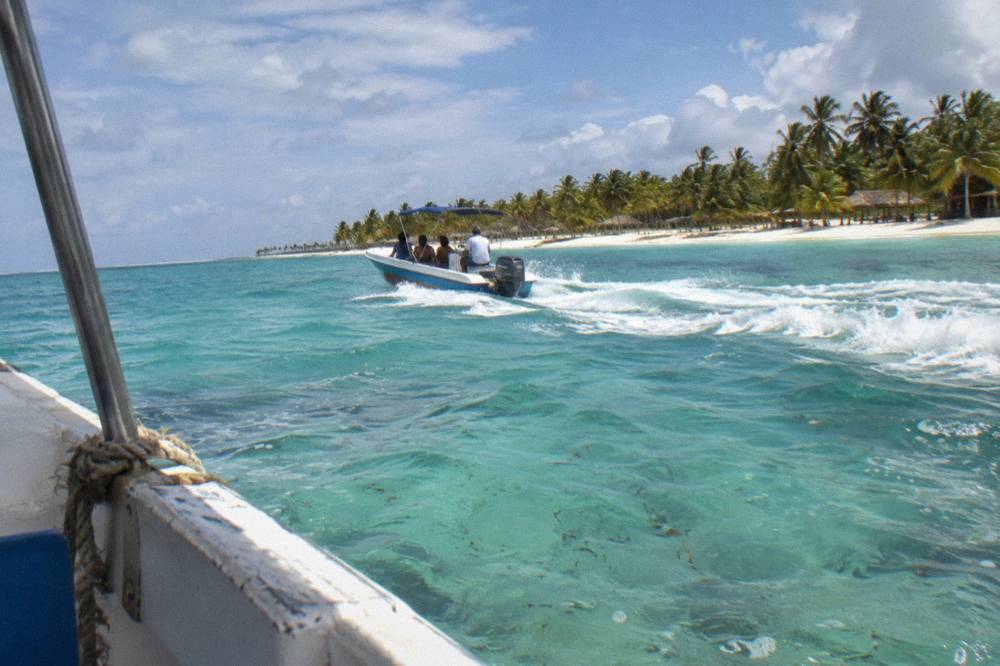 A speedboat cutting across turquoise shallow water toward a sandbank