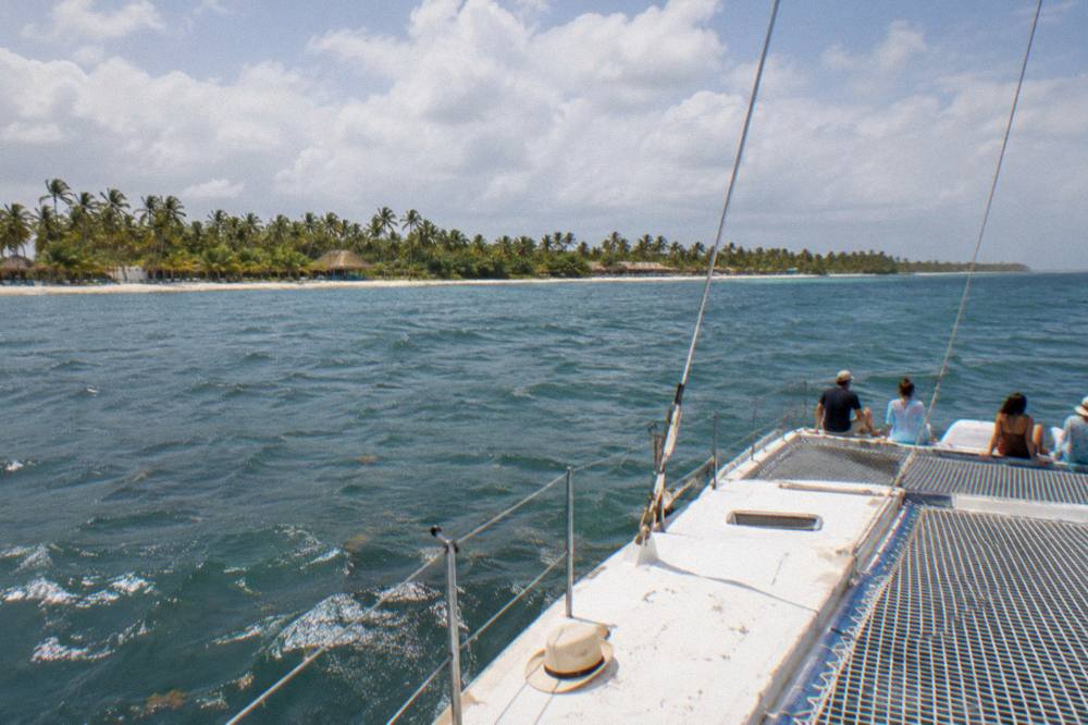 A catamaran under way on calm open water with passengers seated along the trampoline netting