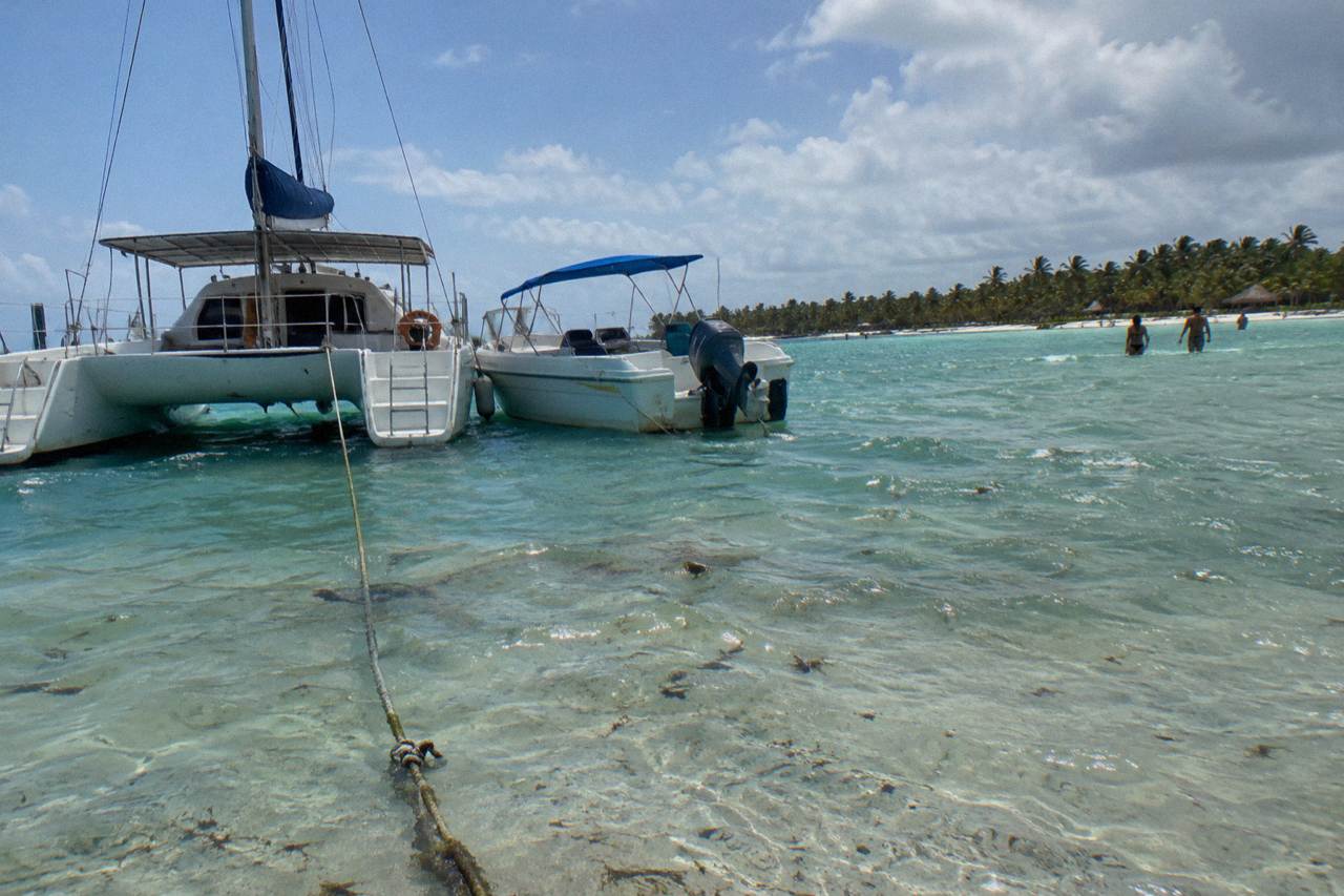 A catamaran and a speedboat moored side by side in turquoise Caribbean water near a sandbar