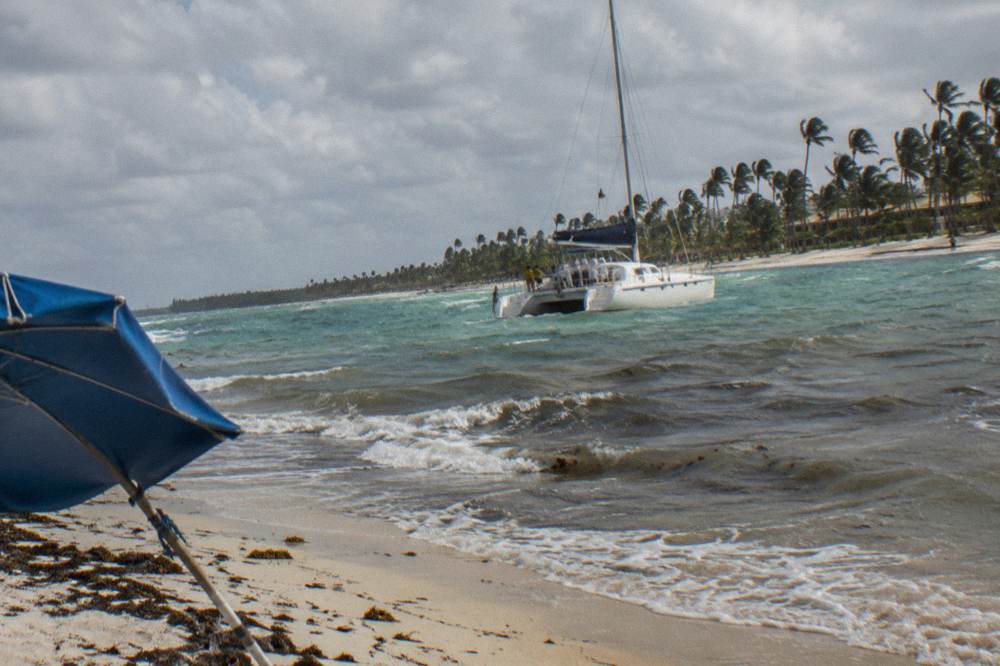 Catamaran under a sky of scattered clouds along a palm-lined Caribbean coast