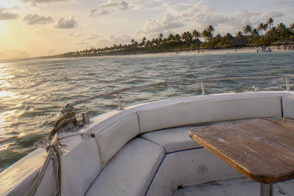 Empty bow area of a moored boat with cushioned seating and a wooden table under an amber late afternoon sky