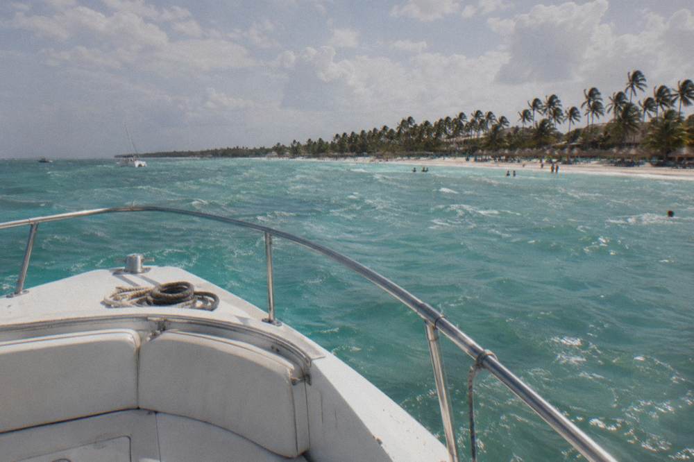 Bow of a small motorboat with a coiled rope heading toward a palm-lined beach