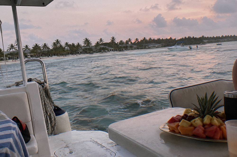 Champagne-style glasses and a fruit platter on the shaded deck of a boat at anchor in early evening light