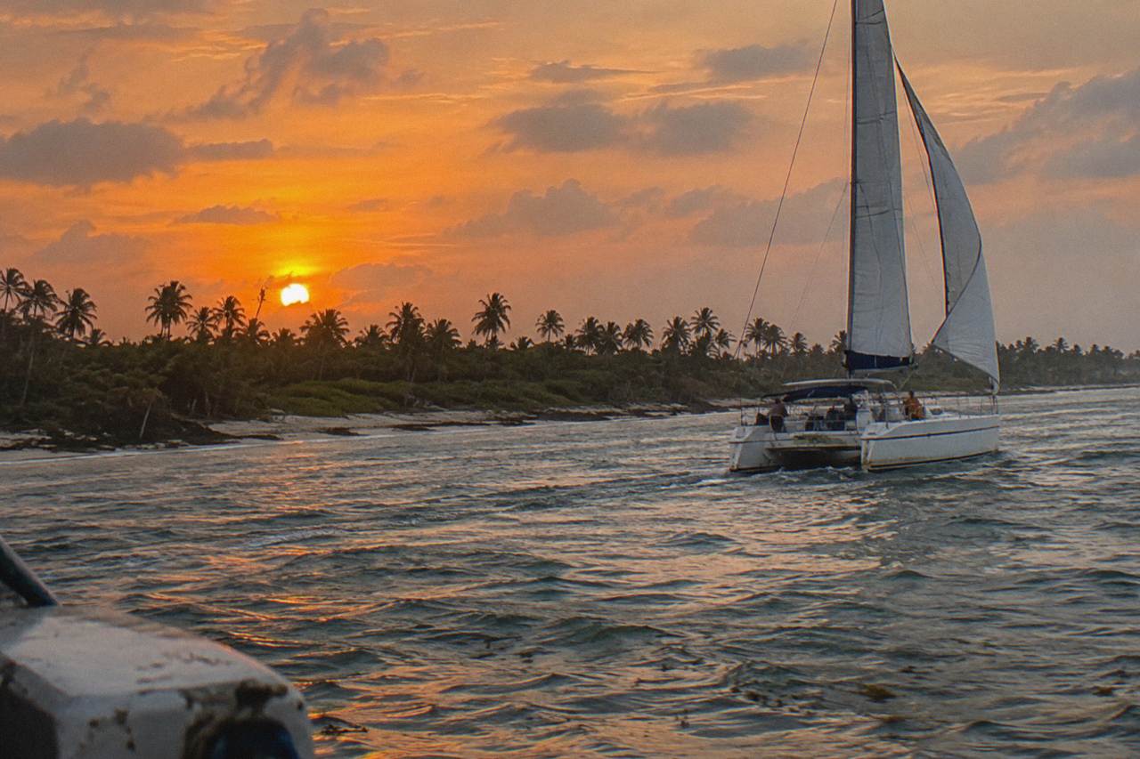 Catamaran sails across calm Caribbean water under a deep orange evening sky near the Punta Cana coast
