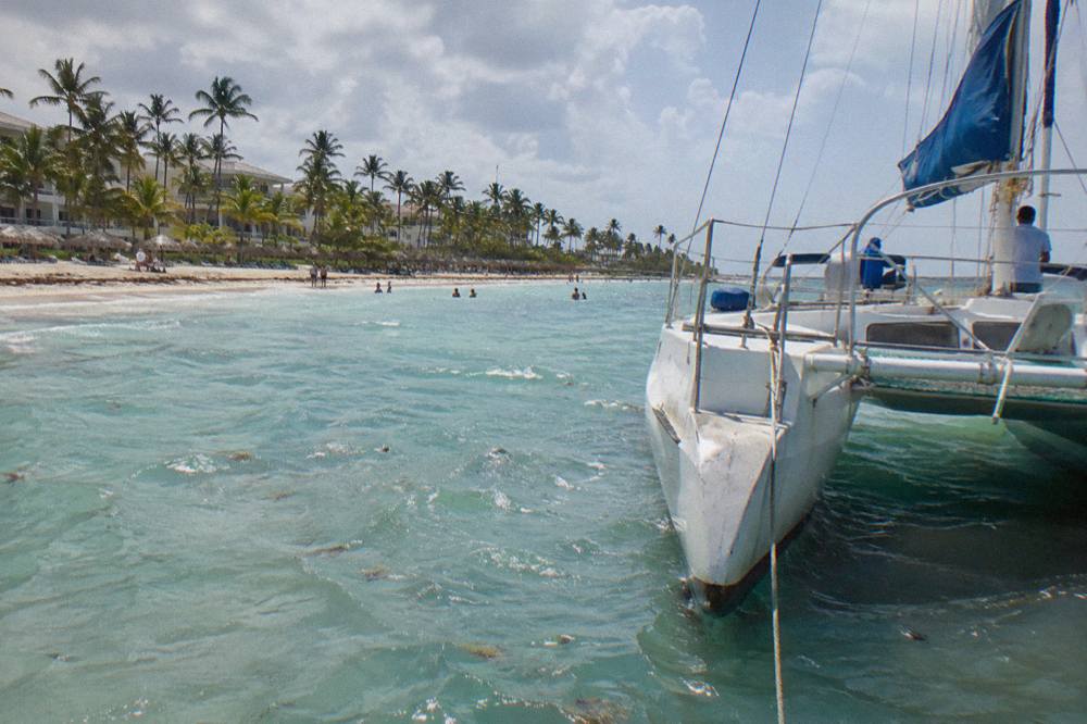 Open-air catamaran moored over clear shallow water near a sandy shoal