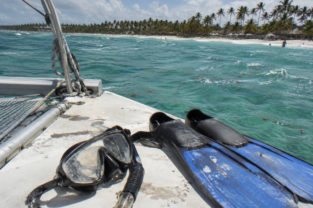 Snorkel fins and mask resting on a boat deck above clear reef water