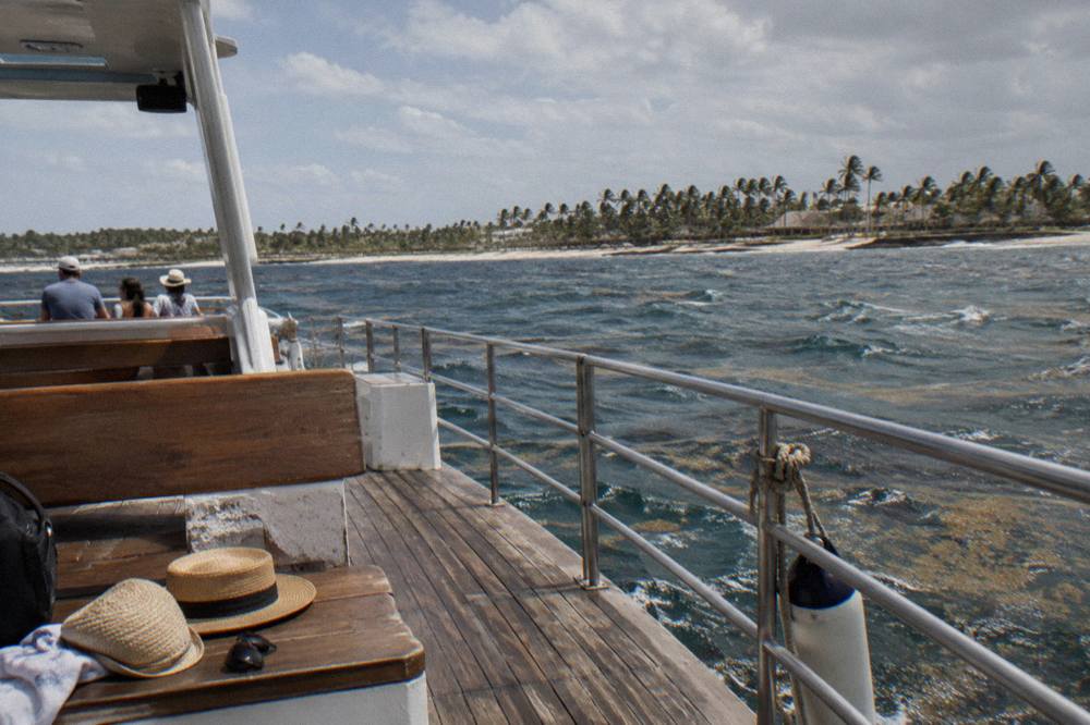 Two straw hats, sunglasses, a towel and a dark backpack on a wooden tour boat bench