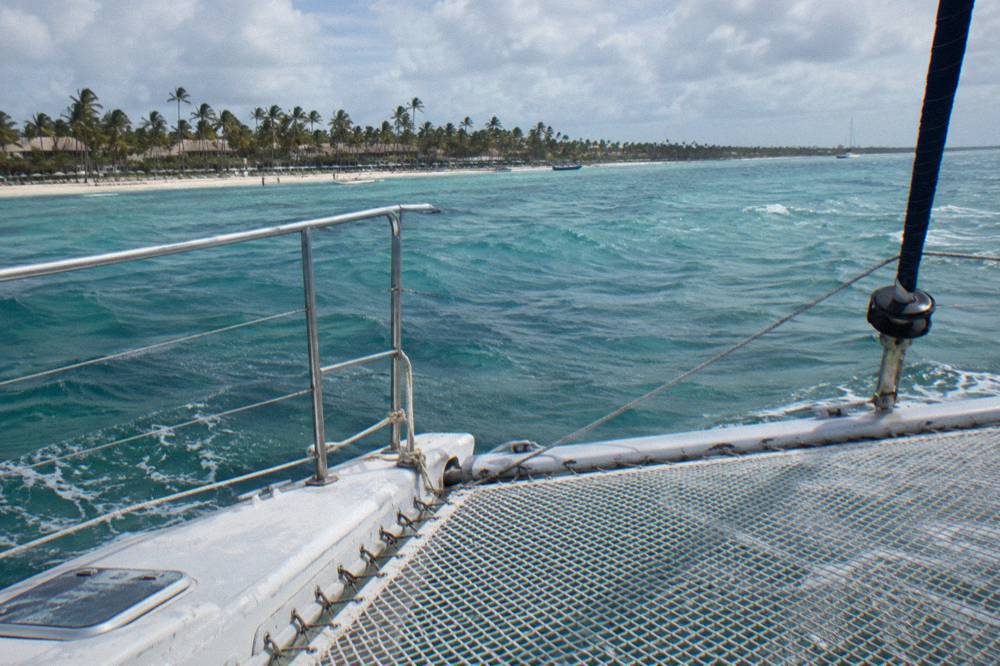 An empty catamaran deck with netting, railings and turquoise sea beyond
