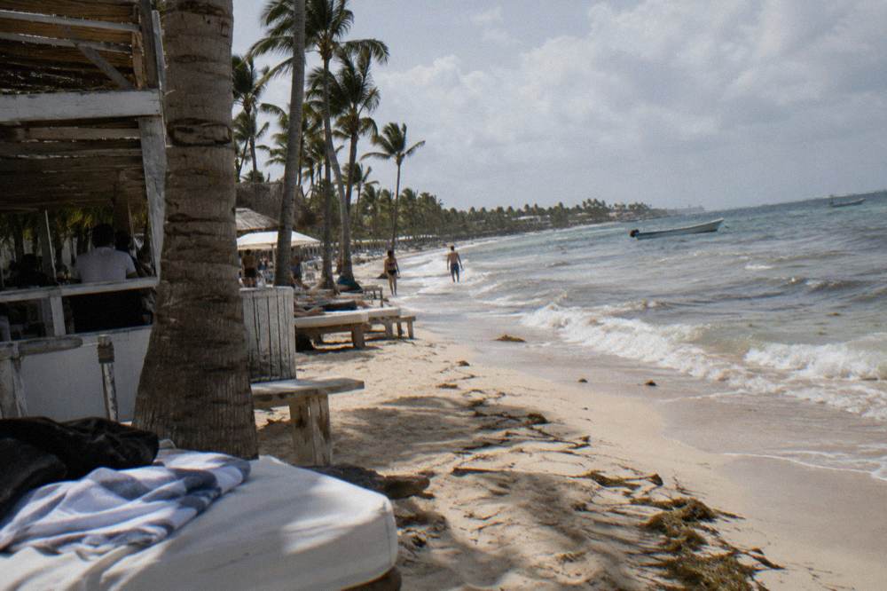 A beach towel and straw hat resting on a sun lounger under palm trees
